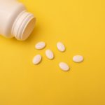 White pills spilling from a bottle on a yellow background