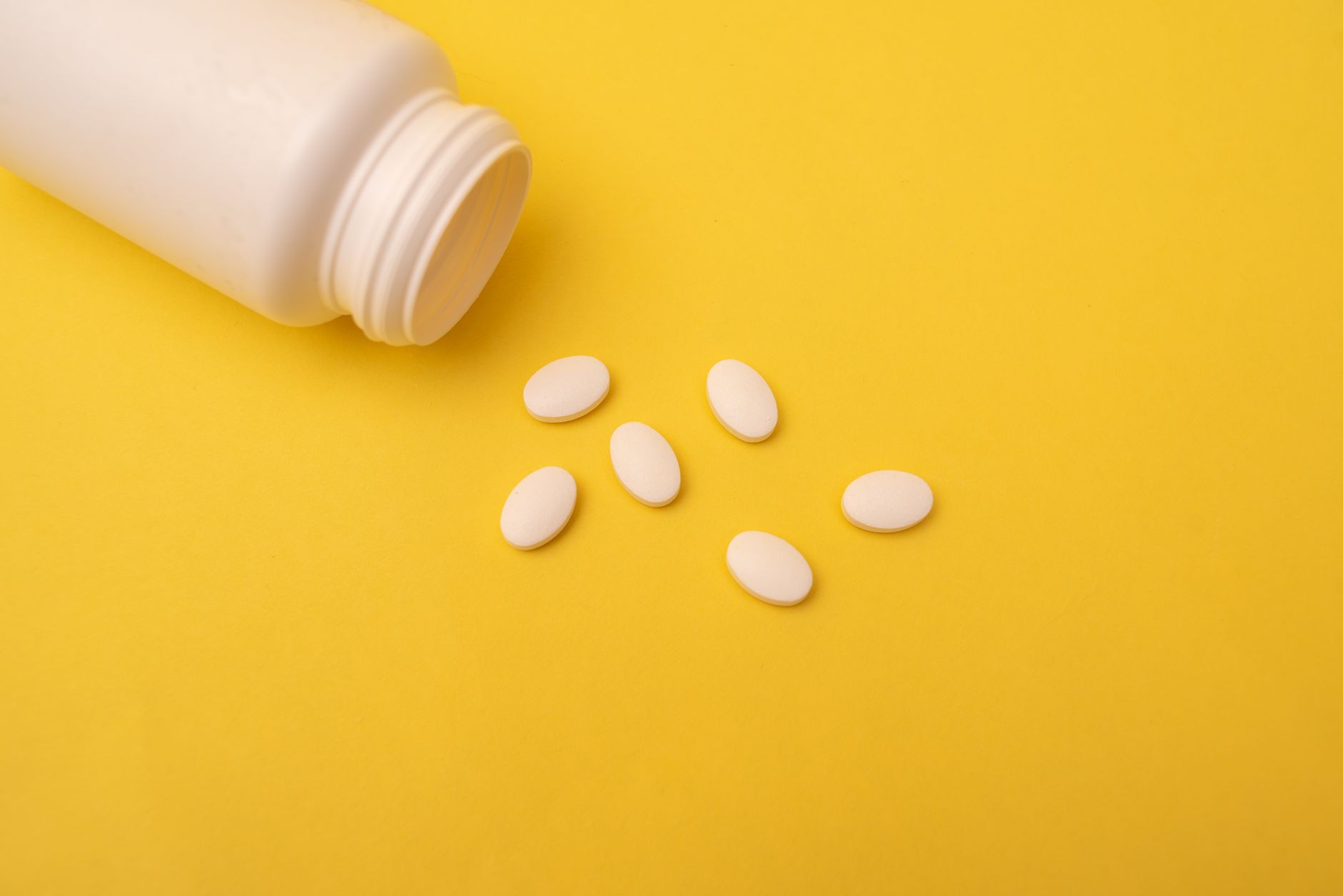 White pills spilling from a bottle on a yellow background
